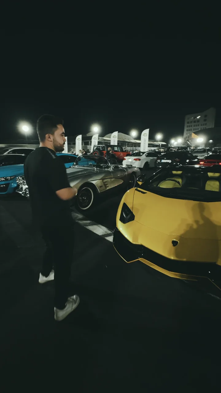 A presenter walking between sports cars at night